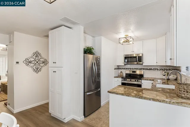 a kitchen with stainless steel appliances granite countertop a refrigerator a stove a sink and white cabinets with wooden floor