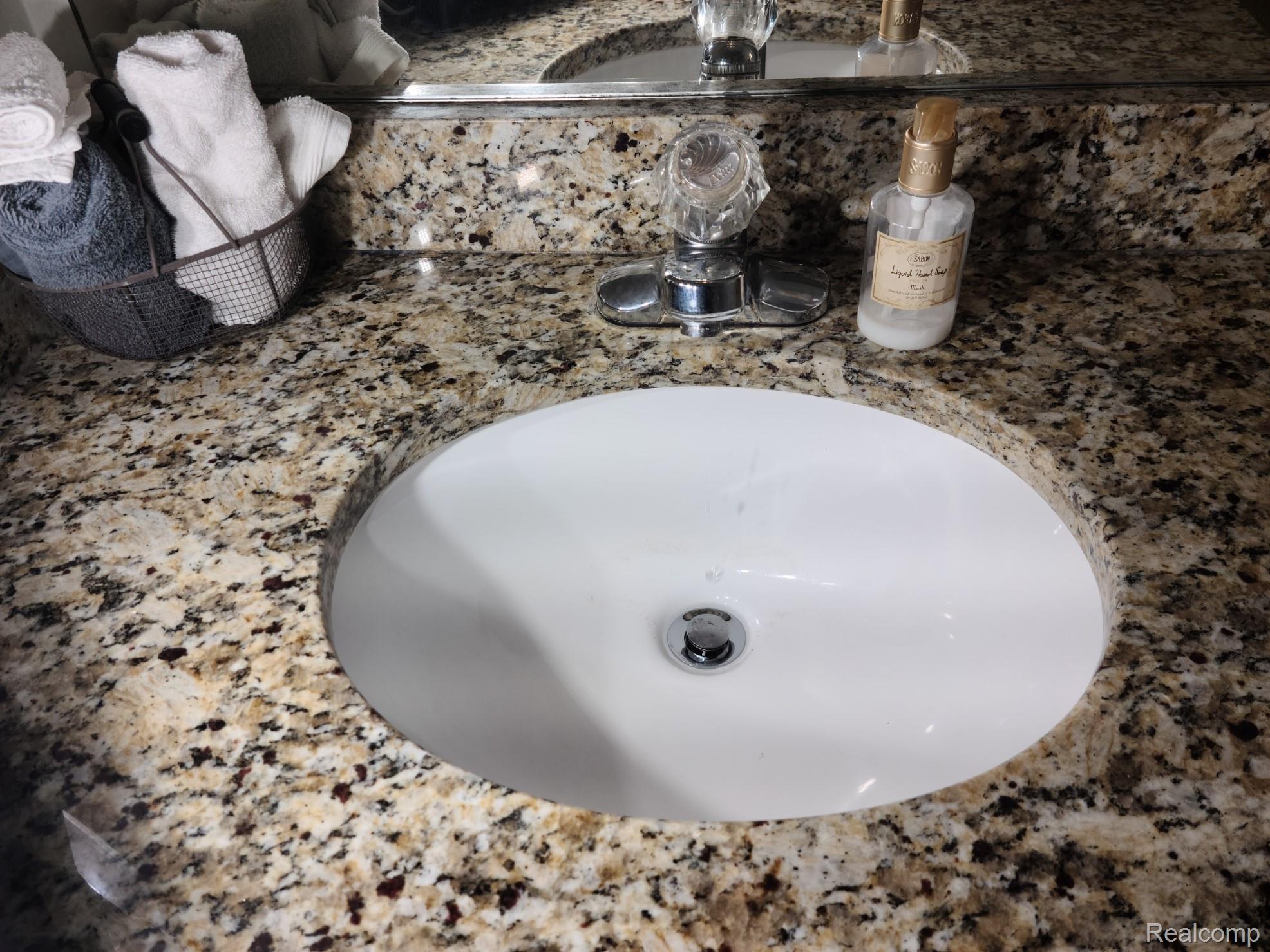 716 Eton Court Rochester, MI 48307 - Photo 22 of 41 Elegant undermount sink with polished white ceramic basin and chrome drain fitting, set within a sophisticated speckled quartz countertop featuring warm bronze and charcoal tones