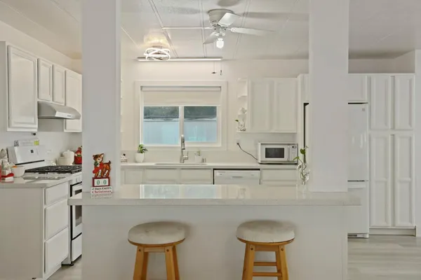 a kitchen with stainless steel appliances granite countertop a sink a stove a refrigerator a window with white cabinets and wooden floor