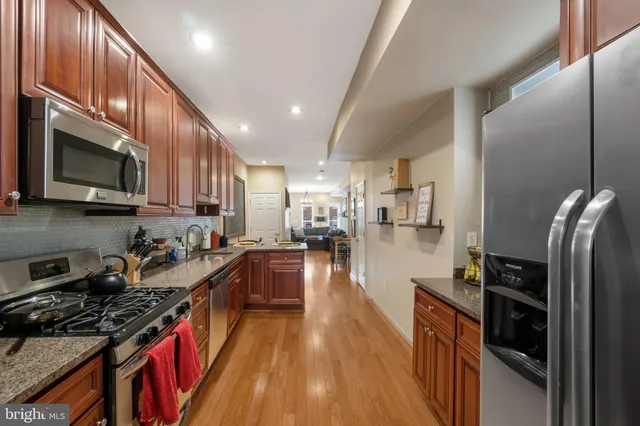 a kitchen with stainless steel appliances granite countertop a stove top oven a sink dishwasher a refrigerator and cabinets with wooden floor