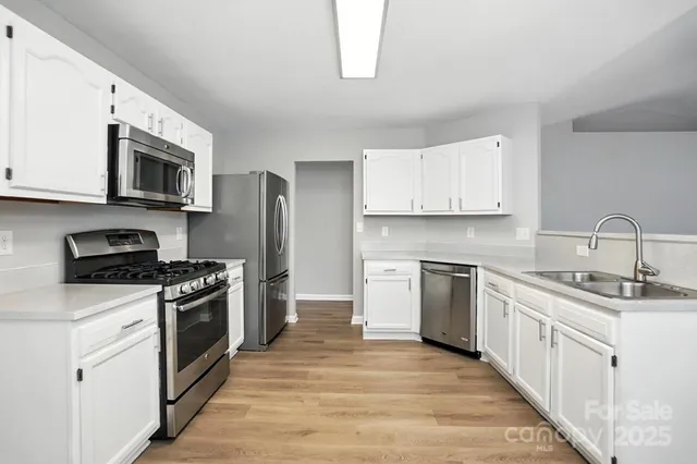 a kitchen with stainless steel appliances granite countertop a stove a sink and white cabinets with wooden floor