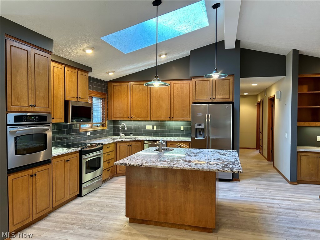 8763 Timber Edge Drive North Ridgeville, OH 44039 - Photo 3 of 40 Kitchen with light hardwood / wood-style flooring, a kitchen island, backsplash, lofted ceiling with skylight, and appliances with stainless steel finishes