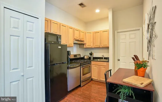 a kitchen with stainless steel appliances granite countertop a refrigerator a stove a sink dishwasher and a dining table with wooden floor