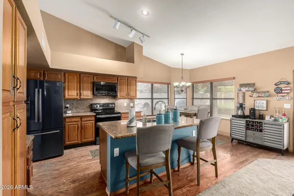 a kitchen with stainless steel appliances granite countertop a stove top oven a refrigerator a dining table and chairs with wooden floor