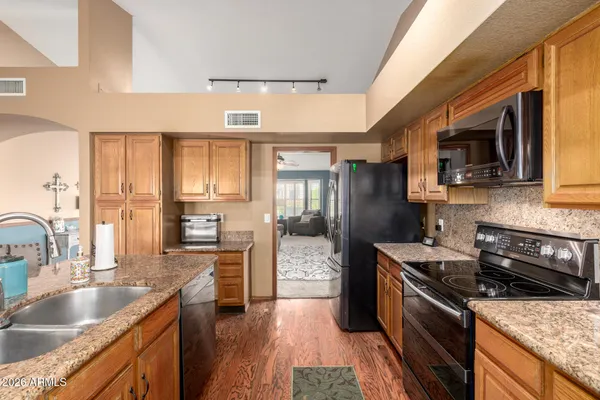 a kitchen with granite countertop stainless steel appliances a sink dishwasher a refrigerator a stove top oven and a dining table with wooden floor