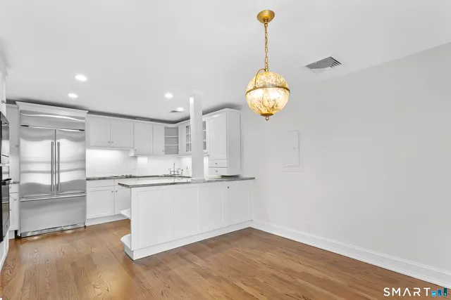 a kitchen with stainless steel appliances granite countertop a sink a stove a refrigerator and white cabinets with wooden floor