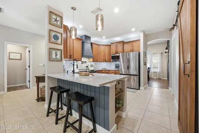 a kitchen with stainless steel appliances kitchen island granite countertop a refrigerator a sink a stove and chairs with wooden floor