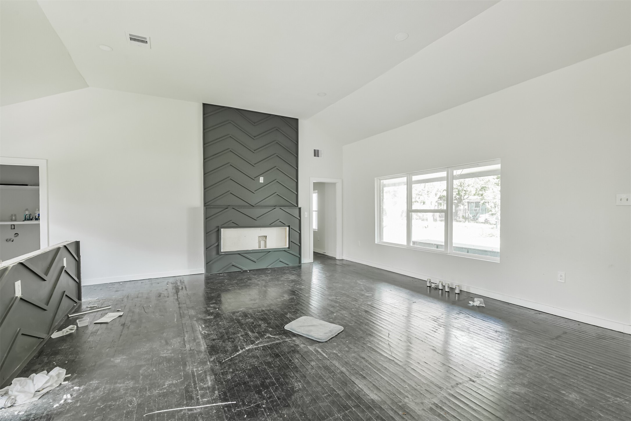 209 Leago Street Houston, TX 77022 - Photo 5 of 24 This photo shows a spacious, modern living room with dark wood flooring and a sleek accent wall featuring a built-in fireplace. Large windows provide ample natural light, and the open layout offers versatile design possibilities.
