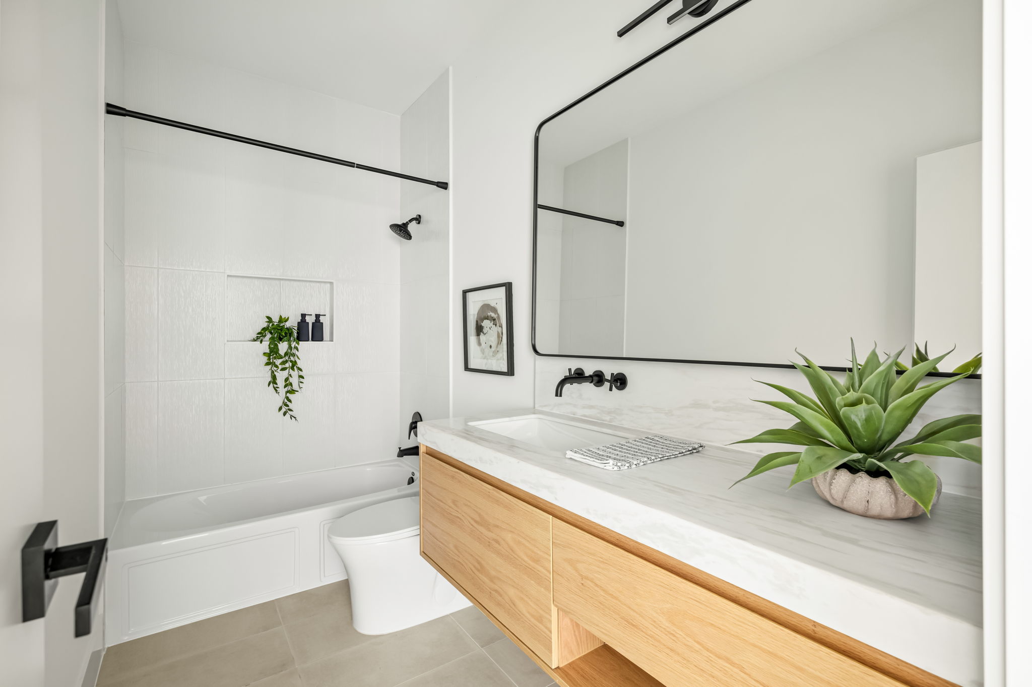 3210 Thompson Street Austin, TX 78702 - Photo 31 of 39 A refined bathroom features a floating vanity with a marble countertop, sleek black fixtures, and a clean white tiled tub-shower combination.