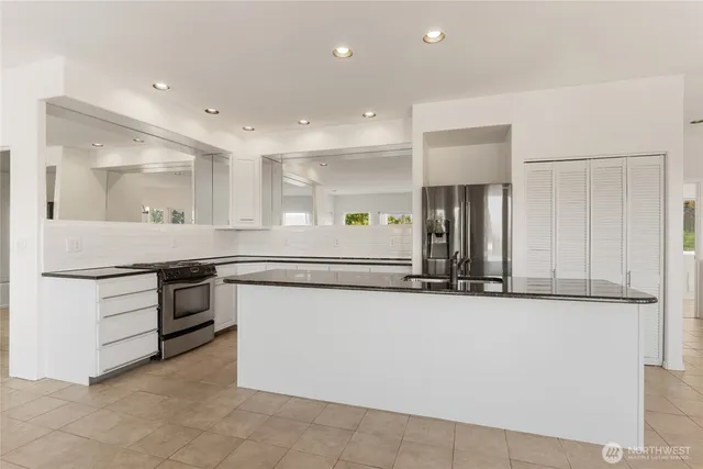 a large white kitchen with stainless steel appliances granite countertop a sink and a stove