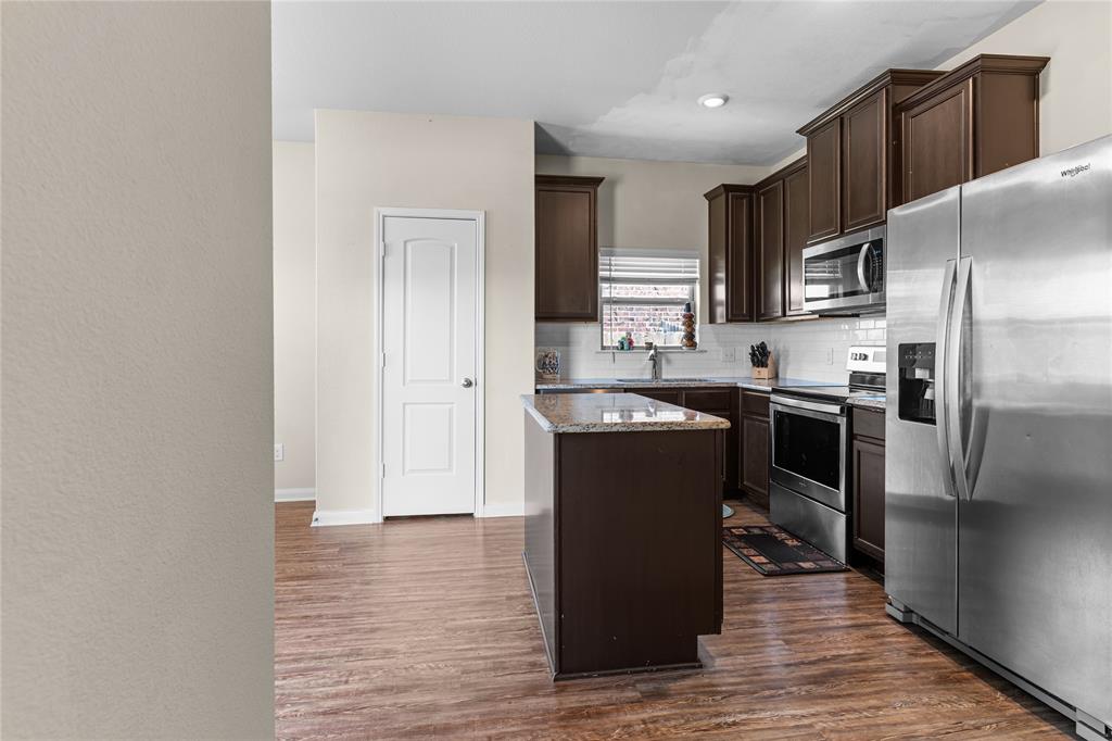 3005 Parker Road Anna, TX 75409 - Photo 4 of 17 Kitchen featuring wood-finish flooring, dark wood cabinetry, a center island with a stone-finish countertop, stainless steel appliances, and a tiled backsplash
