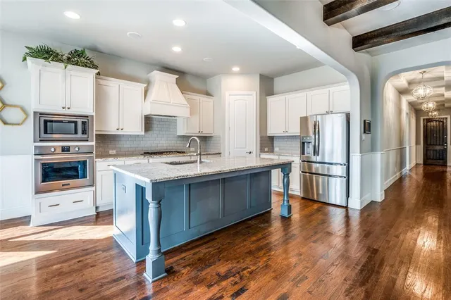 a kitchen with stainless steel appliances granite countertop a refrigerator a stove a sink and a oven with wooden floor