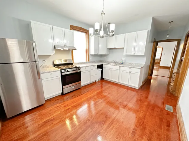 a kitchen with granite countertop a refrigerator a sink dishwasher a stove and white cabinets with wooden floor