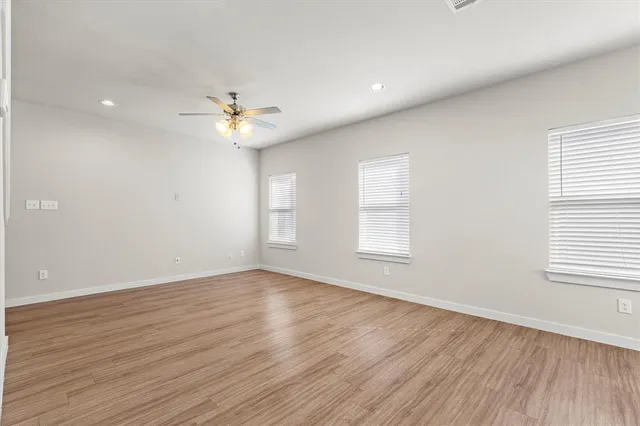 an empty room with wooden floor ceiling fan and windows