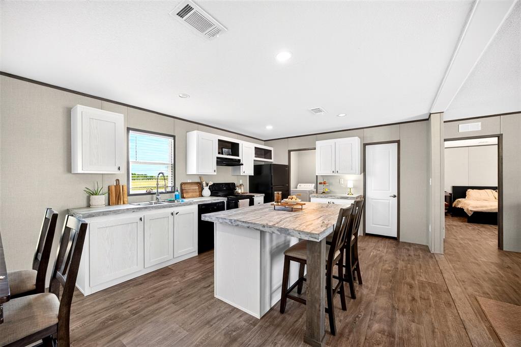 3208 Northeast County Road Powell, TX 75153 - Photo 10 of 29 Kitchen featuring white cabinetry, dark wood-finish flooring, a kitchen island with seating, a stainless steel sink, and black appliances