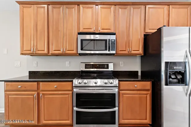 a kitchen with stainless steel appliances granite countertop a refrigerator a sink dishwasher a stove and white countertops with wooden floor