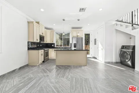 a large white kitchen with stainless steel appliances granite countertop a stove a sink a refrigerator and white cabinets with wooden floor