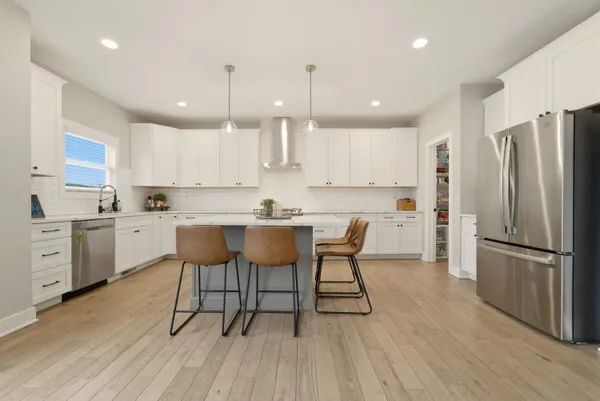 a kitchen with stainless steel appliances granite countertop a refrigerator a sink dishwasher a stove and white cabinets with wooden floor