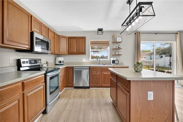 a kitchen with stainless steel appliances granite countertop wooden cabinets a sink a stove a refrigerator and island with wooden floor