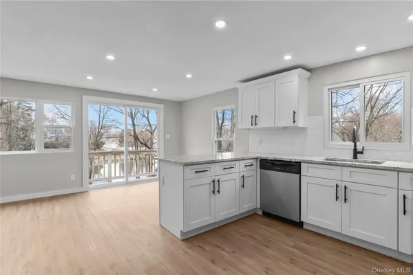 a kitchen with stainless steel appliances granite countertop a stove a sink and white cabinets with wooden floor next to windows