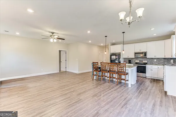a open kitchen with stainless steel appliances kitchen island granite countertop a stove top oven a refrigerator a dining table and chairs with wooden floor