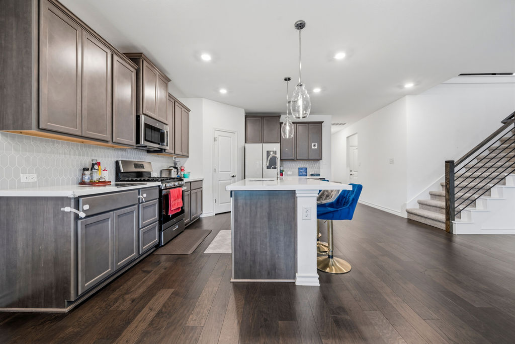 205 Stinchcomb Road Hutto, TX 78634 - Photo 11 of 29 A well-appointed kitchen features stainless steel appliances, an island with seating, and ample cabinetry, all set against rich wood flooring.