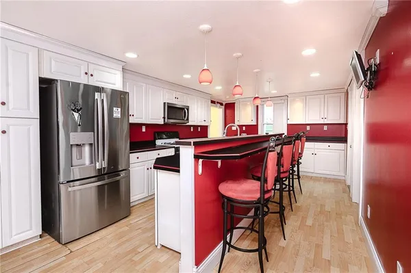 a kitchen with stainless steel appliances kitchen island granite countertop a refrigerator a stove top oven and a dining table with wooden floor