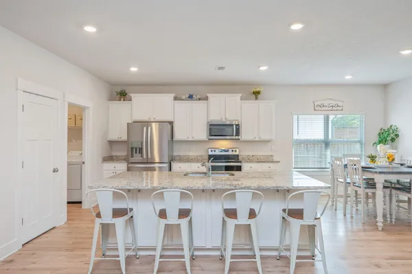 a kitchen with stainless steel appliances granite countertop a dining table chairs refrigerator and microwave