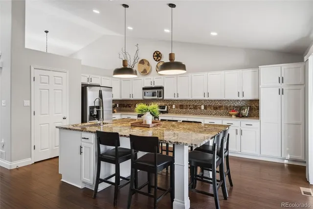 a kitchen with stainless steel appliances granite countertop a stove a refrigerator a kitchen island a sink and white cabinets with wooden floors