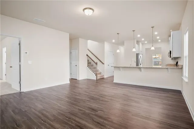 a view of an empty room and kitchen with wooden floor