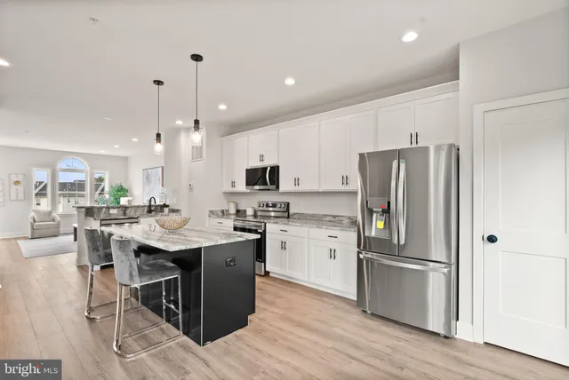 a kitchen with stainless steel appliances kitchen island granite countertop a refrigerator a sink dishwasher a stove and white cabinets with wooden floor