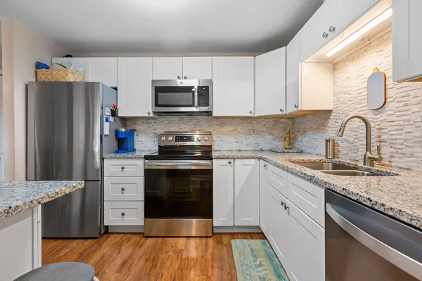 a kitchen with stainless steel appliances granite countertop a stove a sink dishwasher a refrigerator and a microwave oven with wooden floor