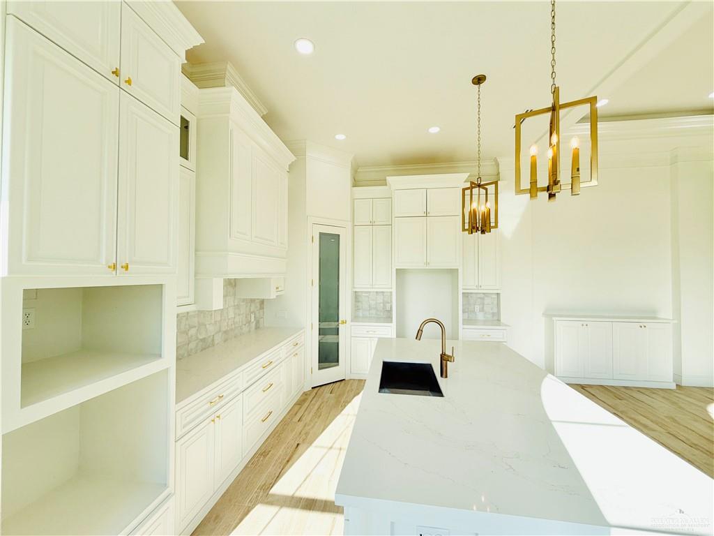 807 Ramirez Street Mission, TX 78573 - Photo 6 of 16 White cabinetry with gold-tone hardware, a large kitchen island with integrated sink, wood tile flooring, and two pendant light fixtures
