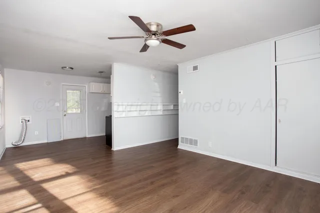 a view of an empty room with wooden floor and a ceiling fan