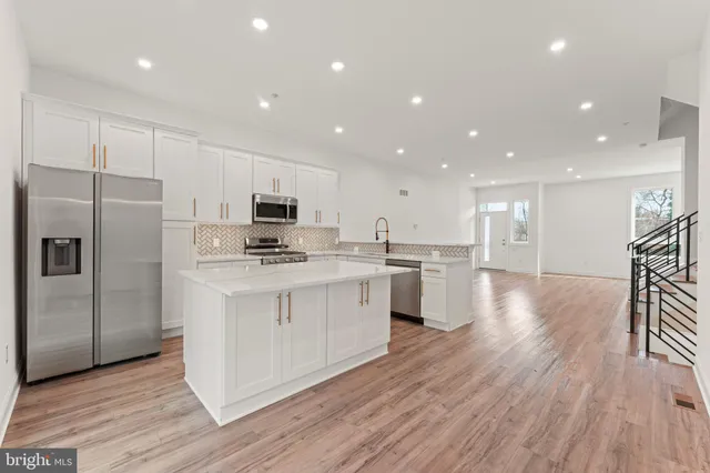 a kitchen with stainless steel appliances kitchen island granite countertop a stove a sink a refrigerator and white cabinets with wooden floor