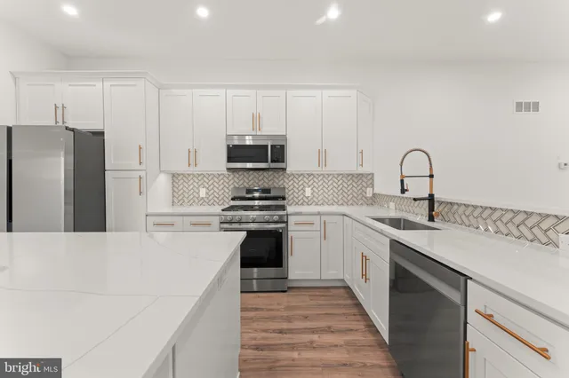 a kitchen with stainless steel appliances a sink dishwasher a refrigerator and a stove with wooden floor