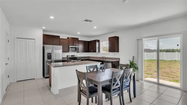 a kitchen with stainless steel appliances granite countertop a stove top oven a sink a refrigerator with a dining table and chairs