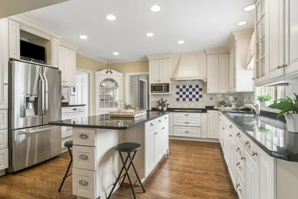 a large white kitchen with granite countertop a stove a sink a refrigerator and white cabinets with wooden floor