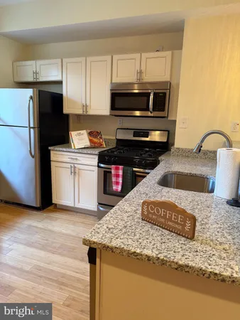 a kitchen with granite countertop a stove a microwave a refrigerator a sink and dishwasher with wooden floor