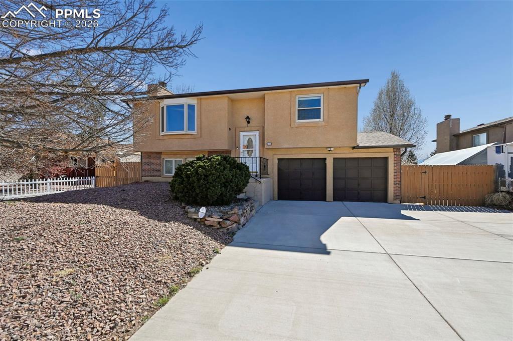 Raised ranch featuring driveway, a garage, stucco siding, brick siding, and a gate