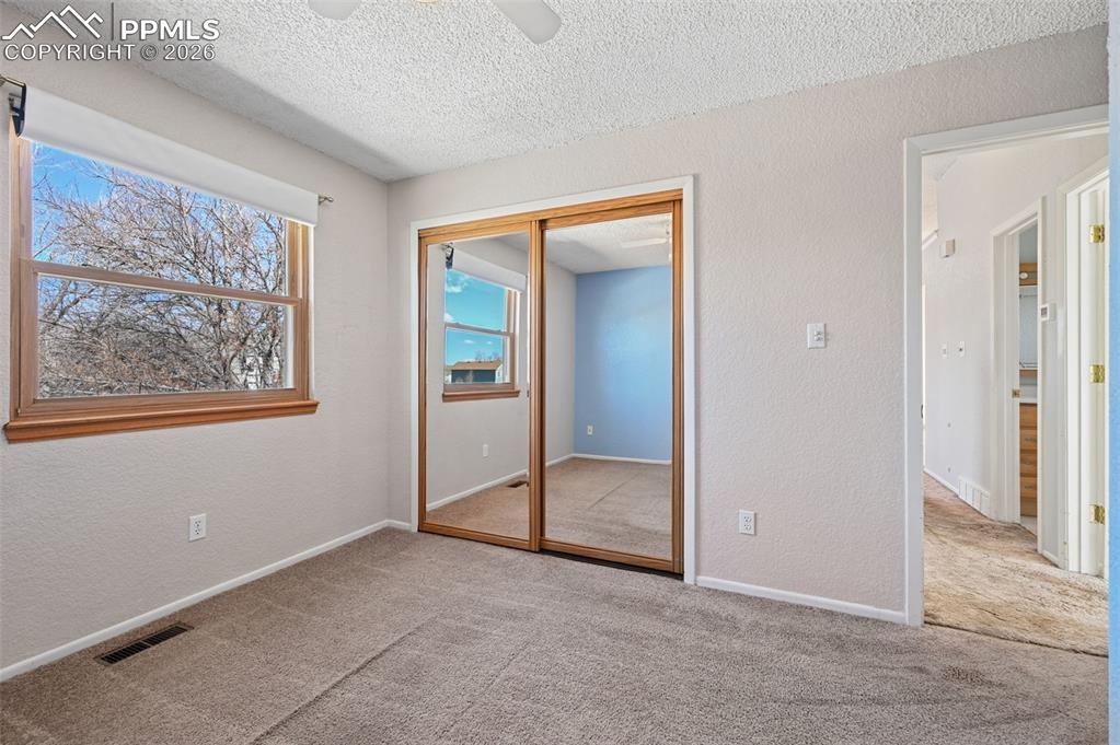 4963 Ridenour Drive Colorado Springs, CO 80916 - Photo 14 of 25 Unfurnished bedroom featuring a textured wall, a textured ceiling, light colored carpet, a closet, and a ceiling fan