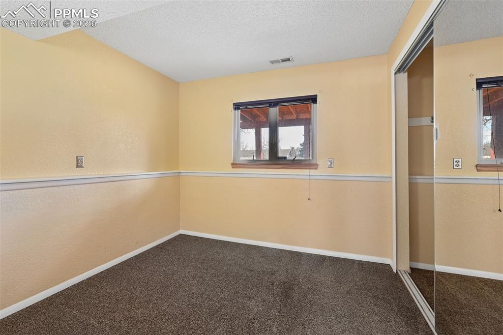 4963 Ridenour Drive Colorado Springs, CO 80916 - Photo 19 of 25 Empty room with a textured wall, dark carpet, and a textured ceiling