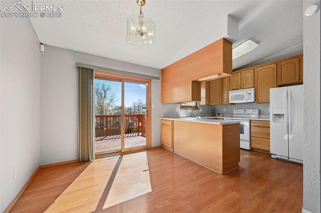4963 Ridenour Drive Colorado Springs, CO 80916 - Photo 7 of 25 Kitchen with light countertops, a peninsula, white appliances, suspended lighting, and light wood-style floors
