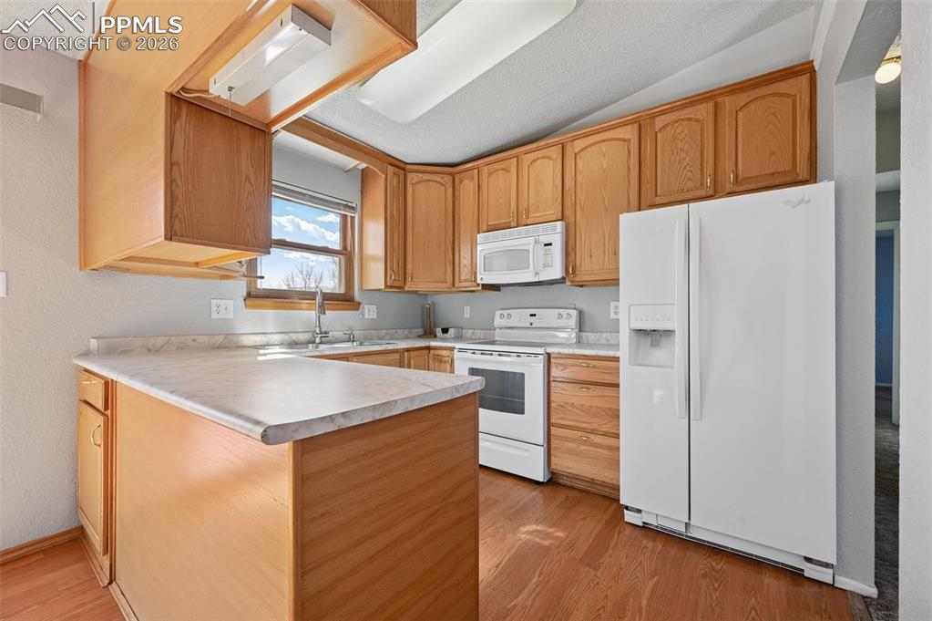 4963 Ridenour Drive Colorado Springs, CO 80916 - Photo 8 of 25 Kitchen with white appliances, light countertops, a peninsula, a textured wall, and light wood-style floors