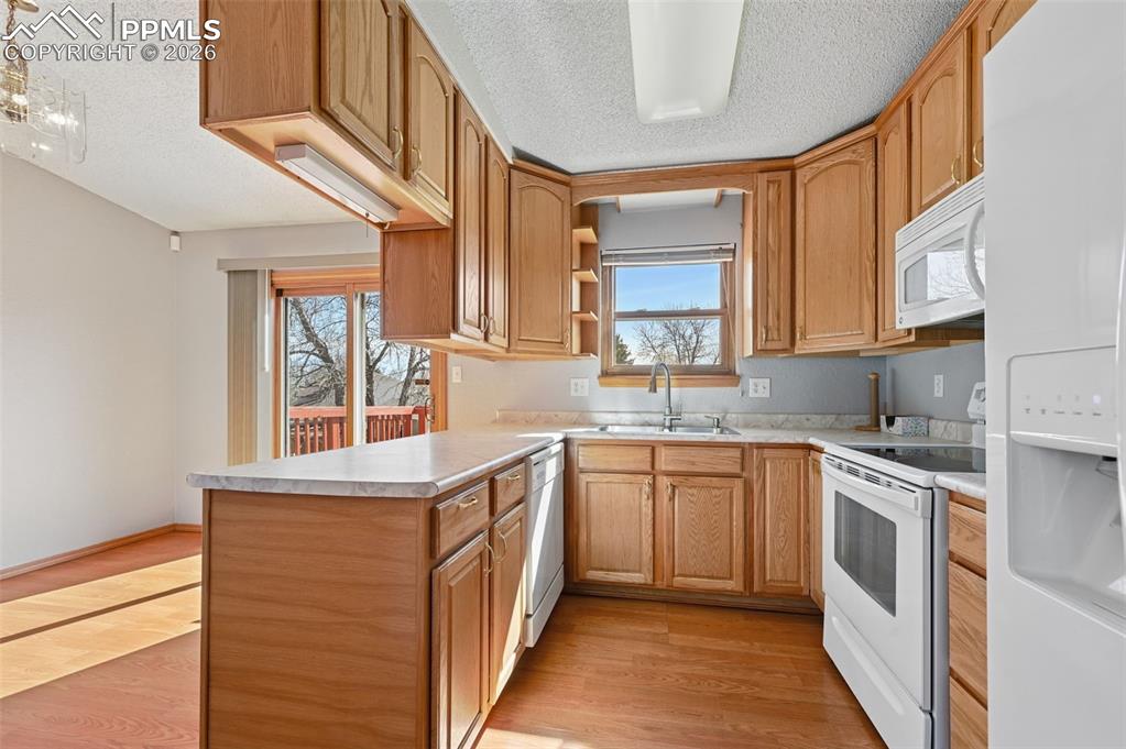 4963 Ridenour Drive Colorado Springs, CO 80916 - Photo 9 of 25 Kitchen featuring white appliances, a peninsula, light countertops, light wood-type flooring, and a textured ceiling