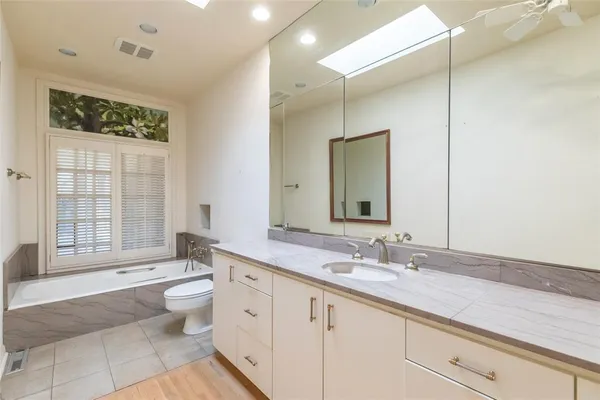 a spacious bathroom with a granite countertop sink toilet a large mirror a bathtub and next to a window