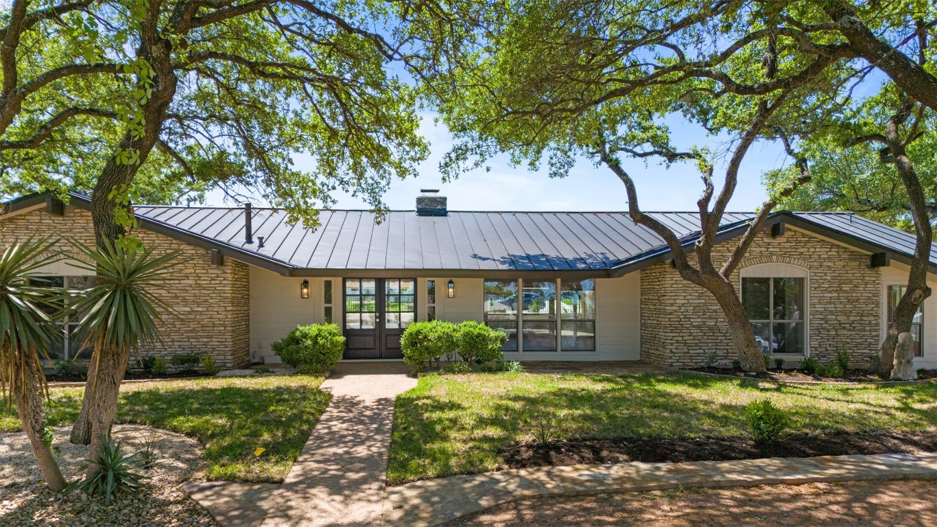 This stunning home features a modern metal roof, beautiful stone accents, and large windows, all set amidst a landscaped yard with mature trees, offering great curb appeal and a welcoming entrance.