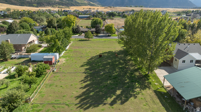 Expansive grass lot with mature trees, mountain backdrop, and multiple outbuildings