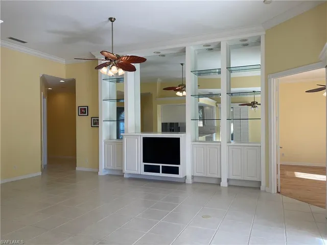 an empty room with chandelier fan and kitchen view