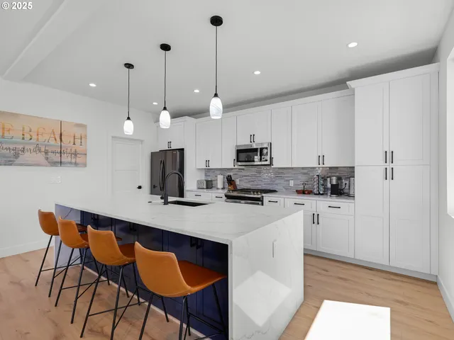 a kitchen with stainless steel appliances kitchen island granite countertop a sink a stove a refrigerator and white cabinets with wooden floor